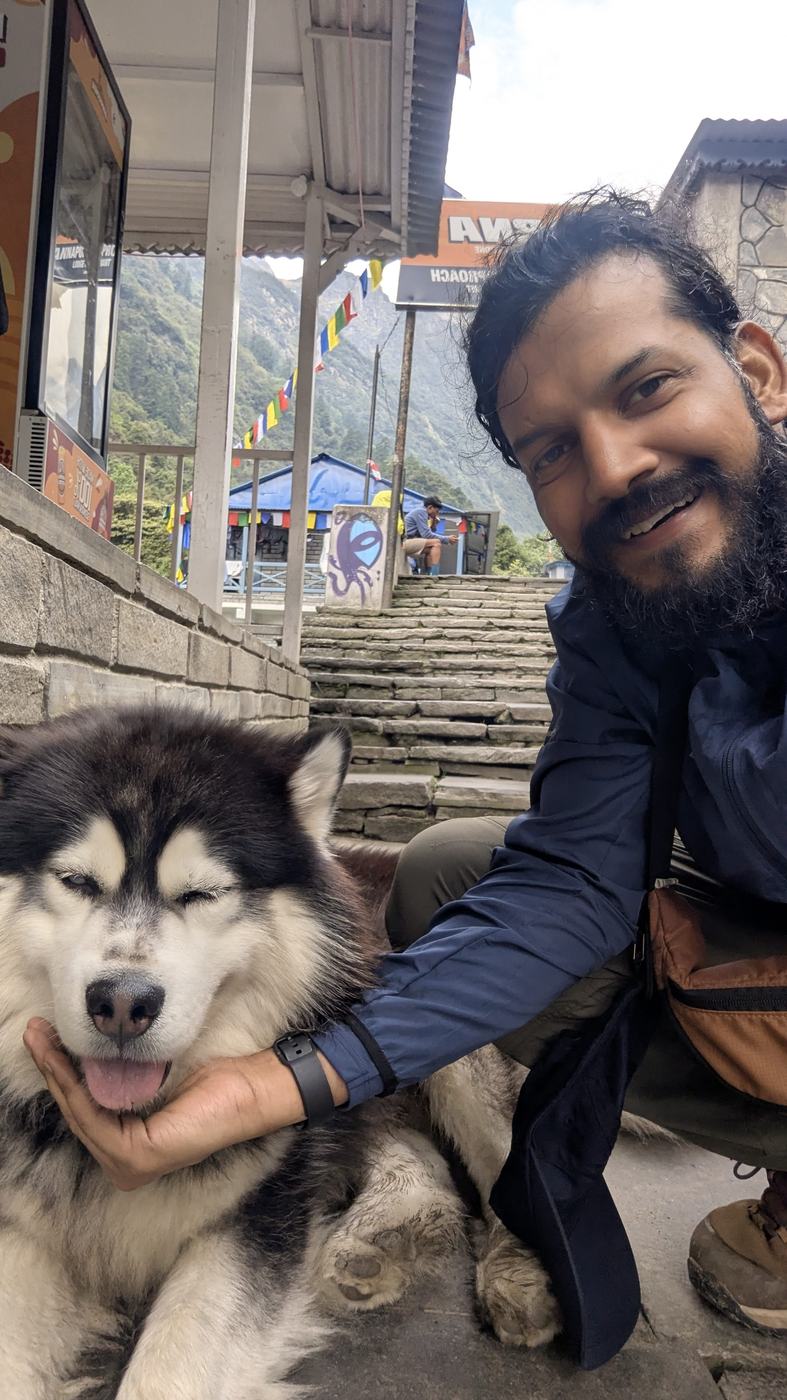 Anurag sitting with a husky on a mountain trail