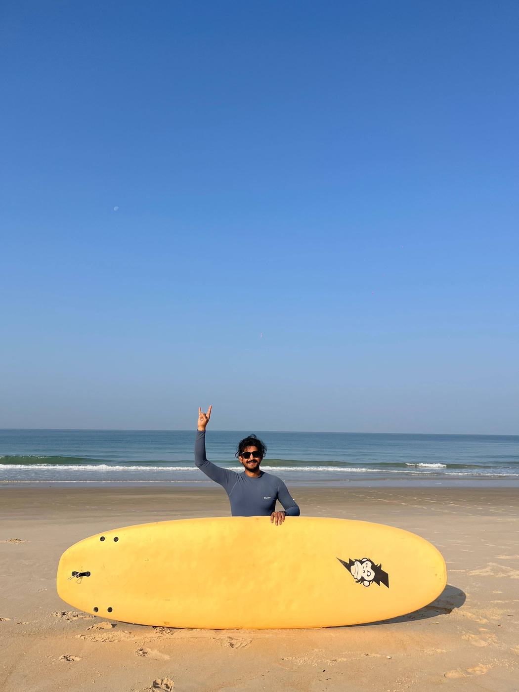 Anurag on a beach with a yellow surfboard